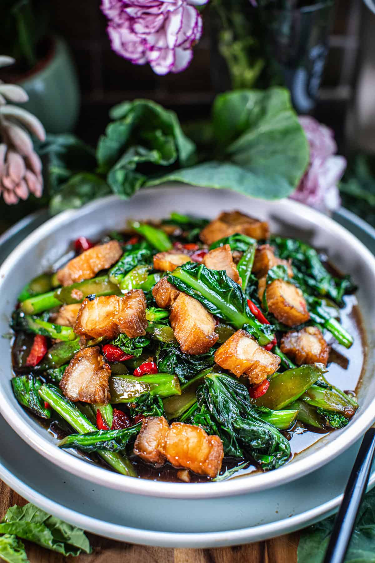 Kana Moo Grob stir fry on a plate with greens around it.