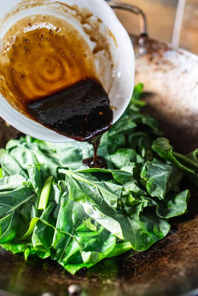 Sauce pouring into Chinese broccoli leaves in a wok for Thai  pad kana recipe.