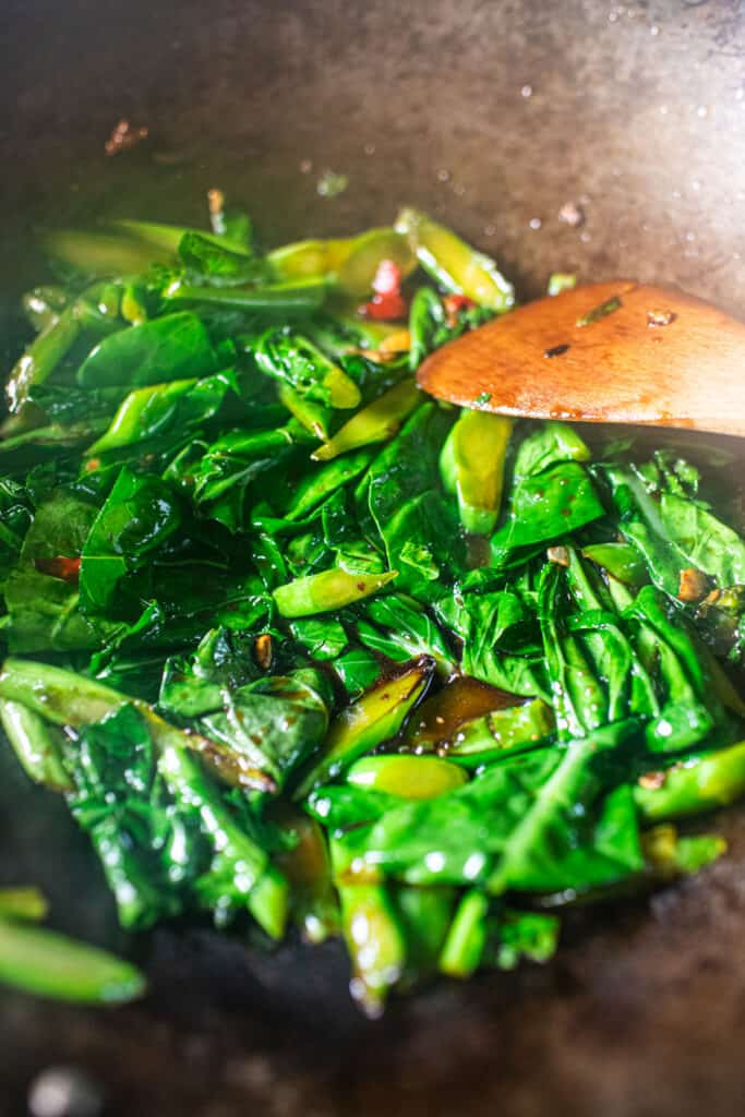 Spatula stirring Chinese broccoli leaves in a wok.
