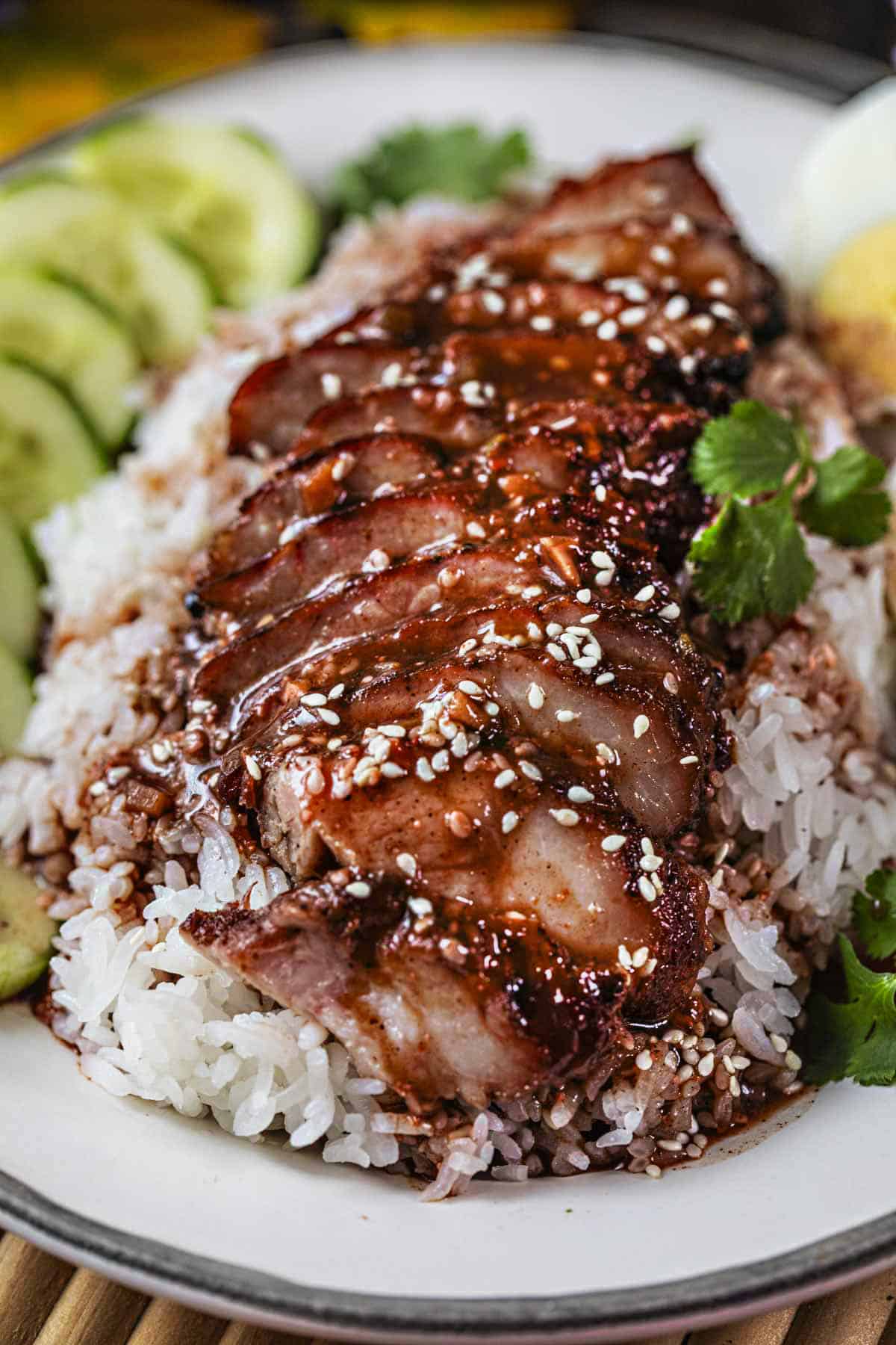 Red pork slices on top of rice with red sauce and sesame seeds on top.