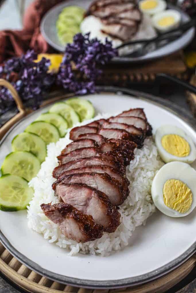 kao moo dang pork slices over rice with eggs and cucumber slices. 