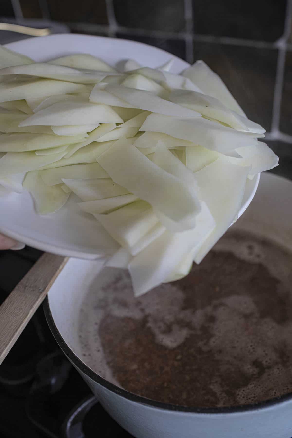 raw green papaya pouring into a soup pot. 