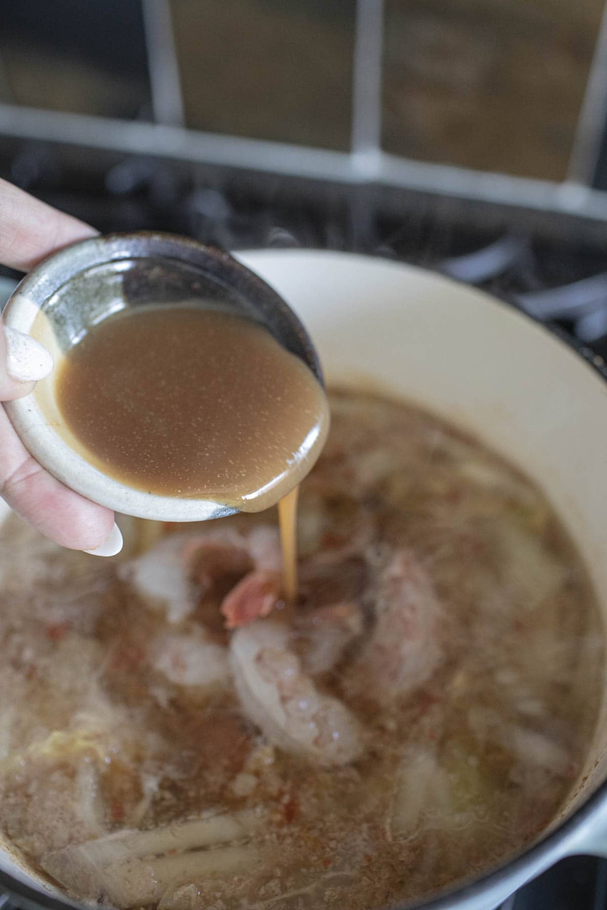 Tamarind juice pouring into a soup pot on the stove. 