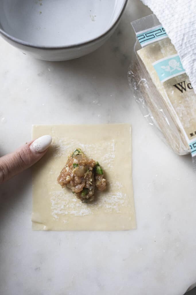 Finger pointing at a wonton wonton on a cutting board. 