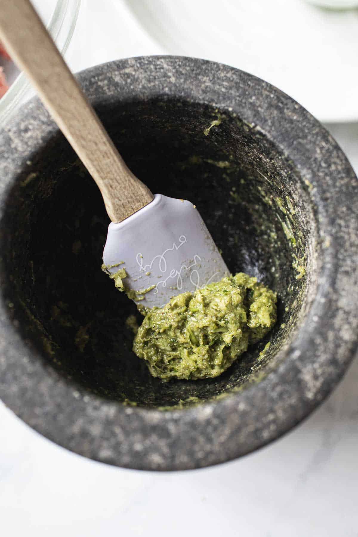 Spatula lifting green paste from a mortar. 