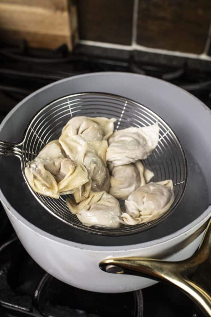 shrimp wontons in a wiremesh strainer over a pot of water. 