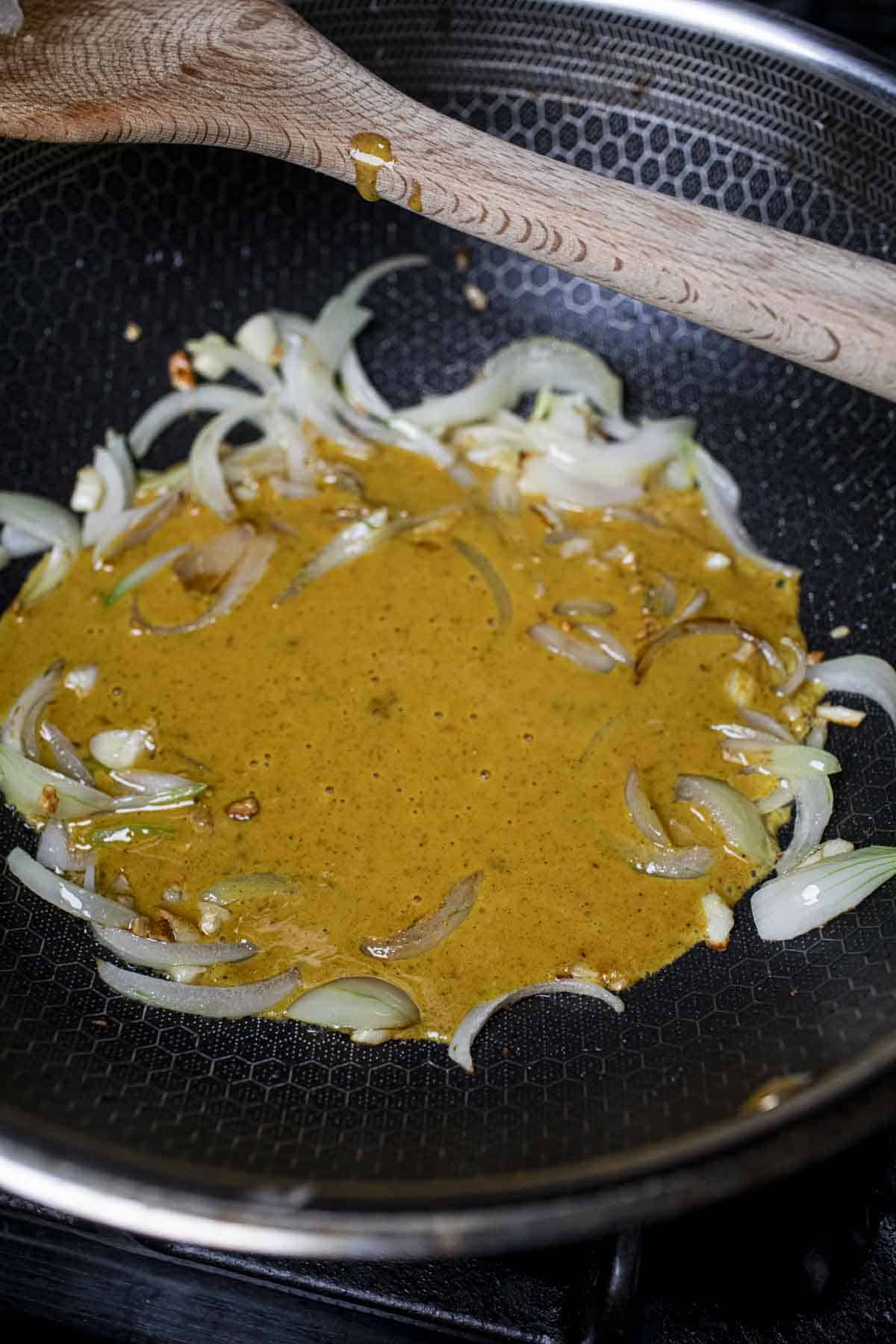 Onion and creamy yellow sauce in a wok on the stove. 