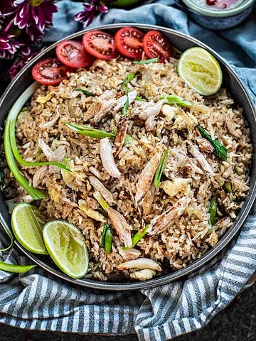 Thai crab fried rice on a plate with tomato and lime wedges.