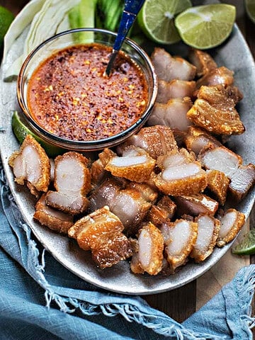 Thai Crispy Pork belly slices on a platter with hot sauce.