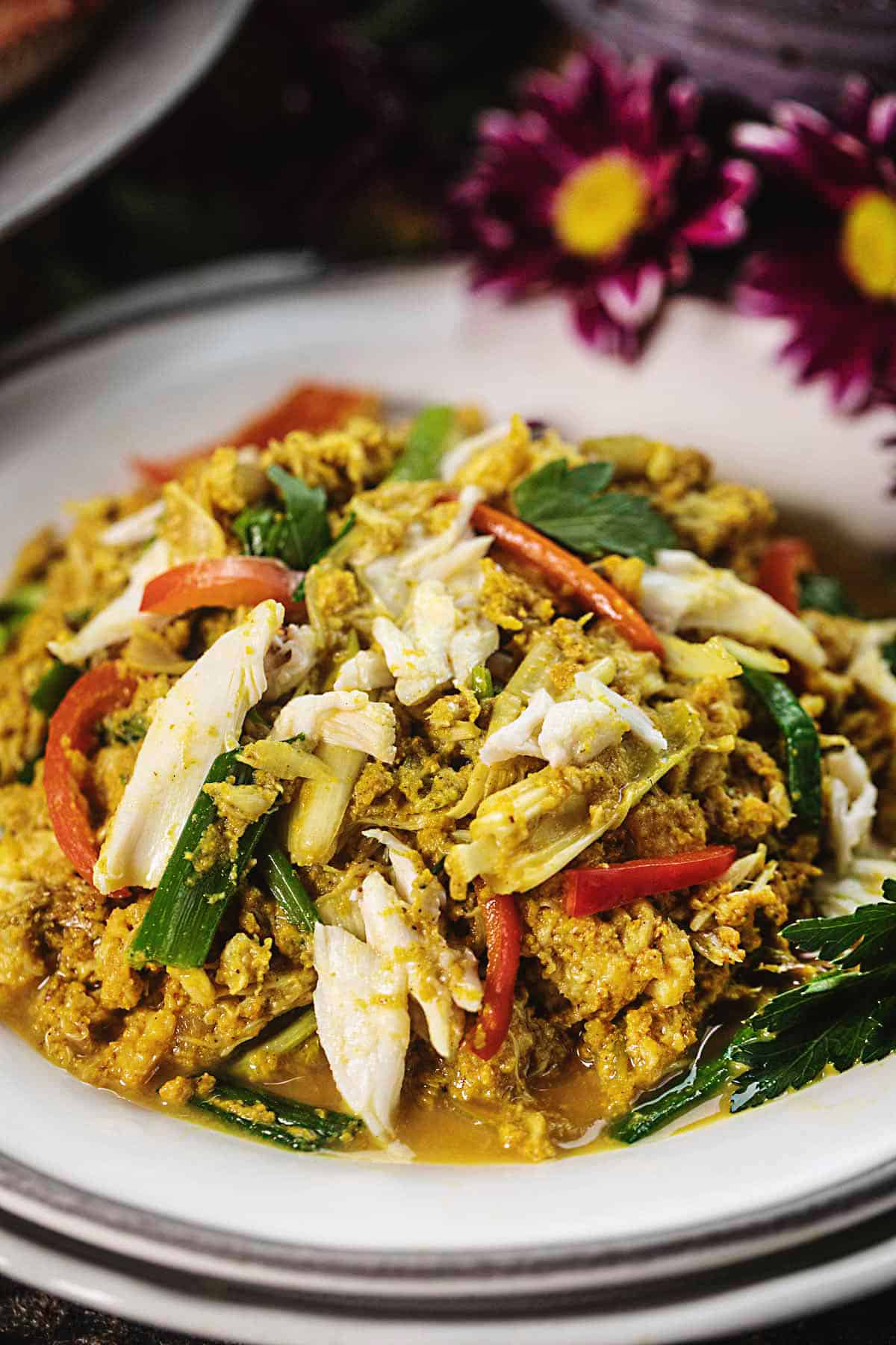 Pad Pong Karee crab stir fry on a white platter with flowers on the side. 