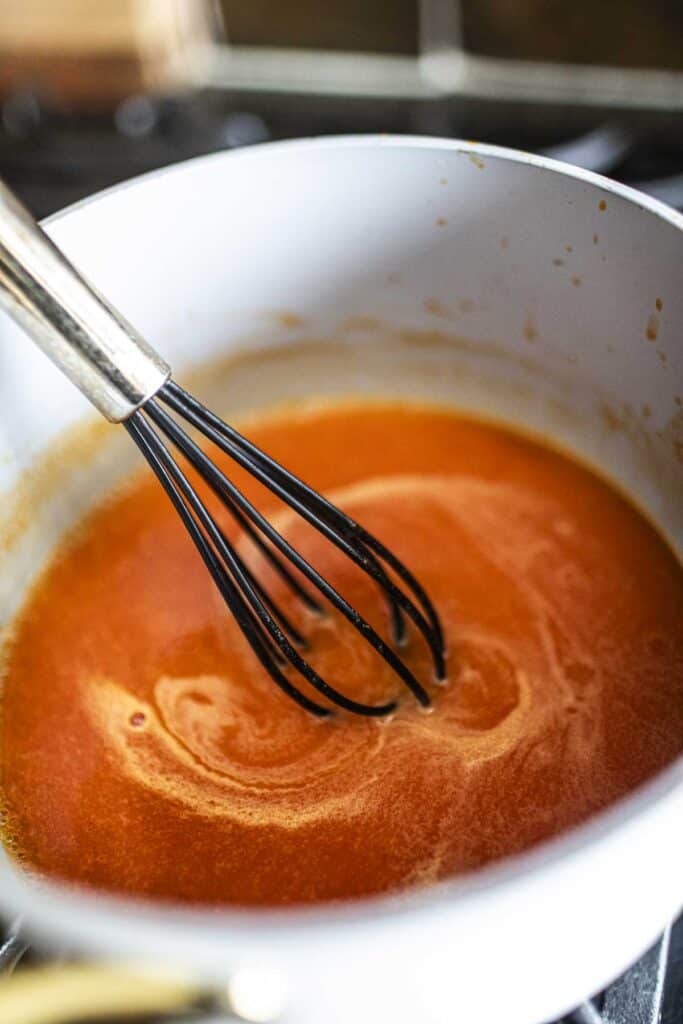 A whisk in a sauce pan stirring homemade sriracha sauce.