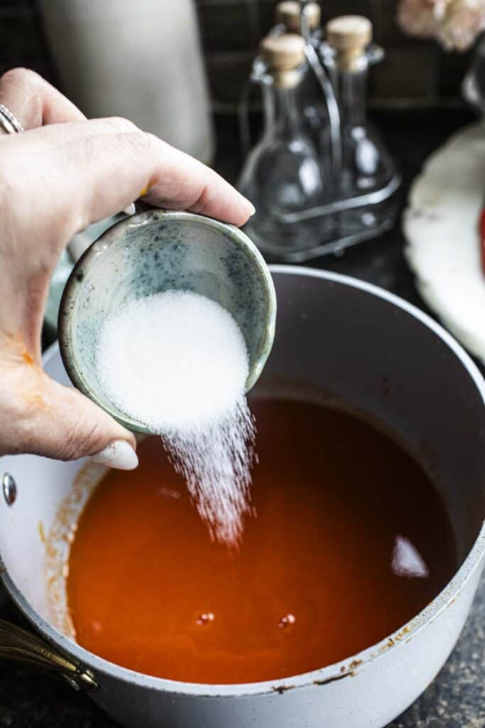 Sugar pouring into a sauce pan stirring homemade thai sriracha sauce.