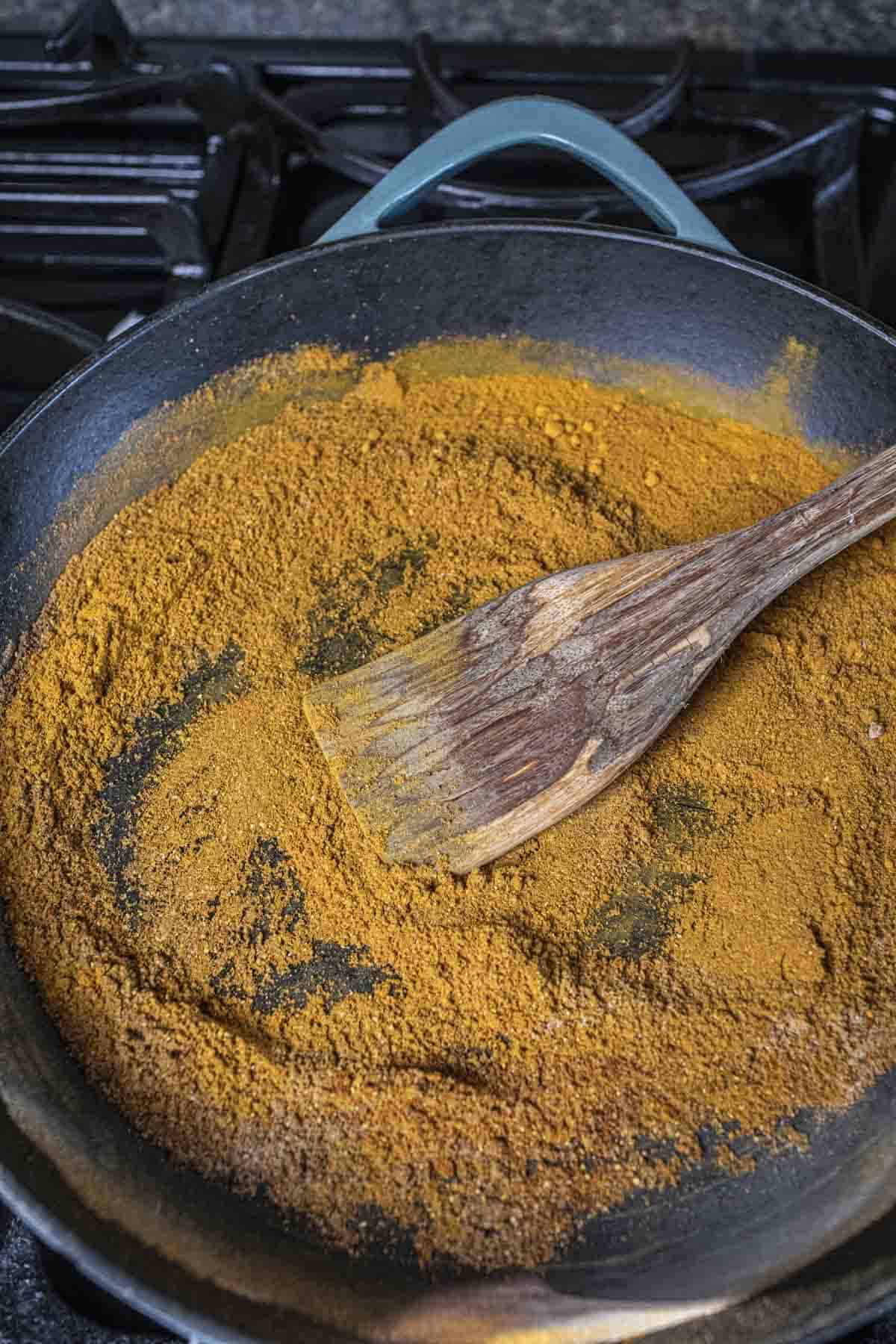 Yellow curry powder blends in a pan on the stovetop.