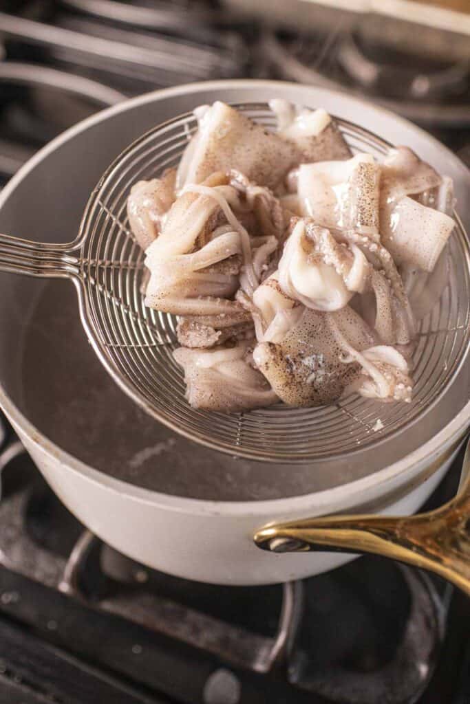 Slotted spoon with squid pieces inside a pot of boiling water.