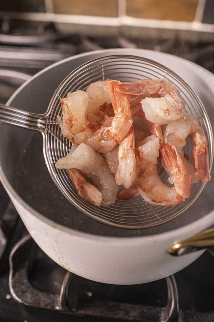 Slotted spoon with shrimp  inside a pot of boiling water.