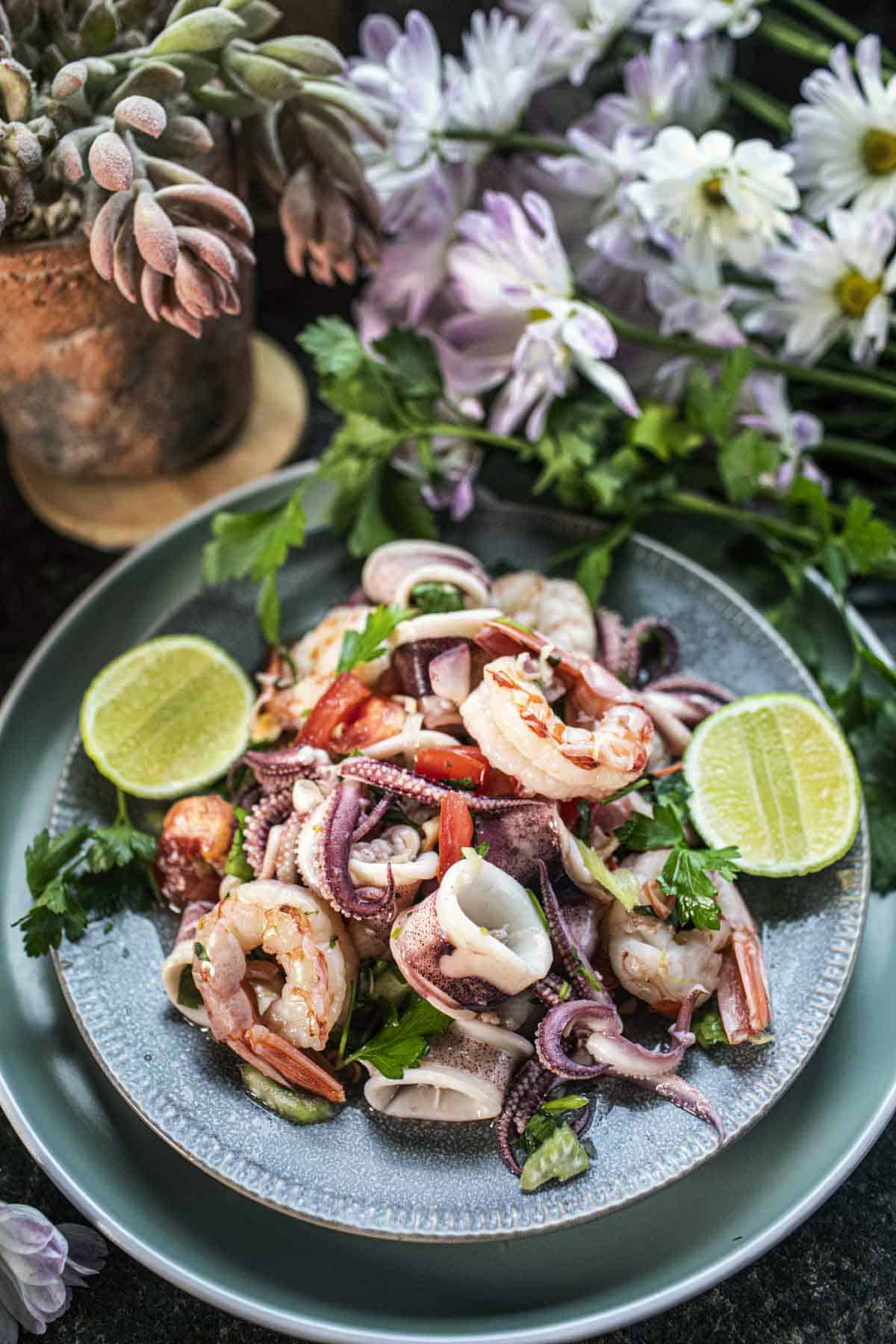 Thai Yum Talay with shrimp and squid on a plate with lime wedges.