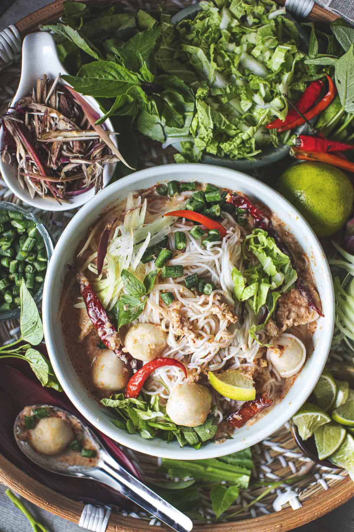 Kanom Jeen Nam Ya Curry in a bowl with vegetables around. 