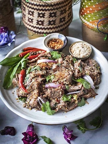 Moo NAM TOK salad on a plate with roasted rice and chilies.