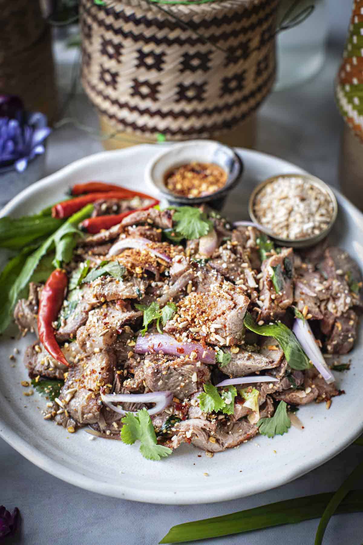 Nam Tok Moo salad on a plate with chilie and lime garnishes. 