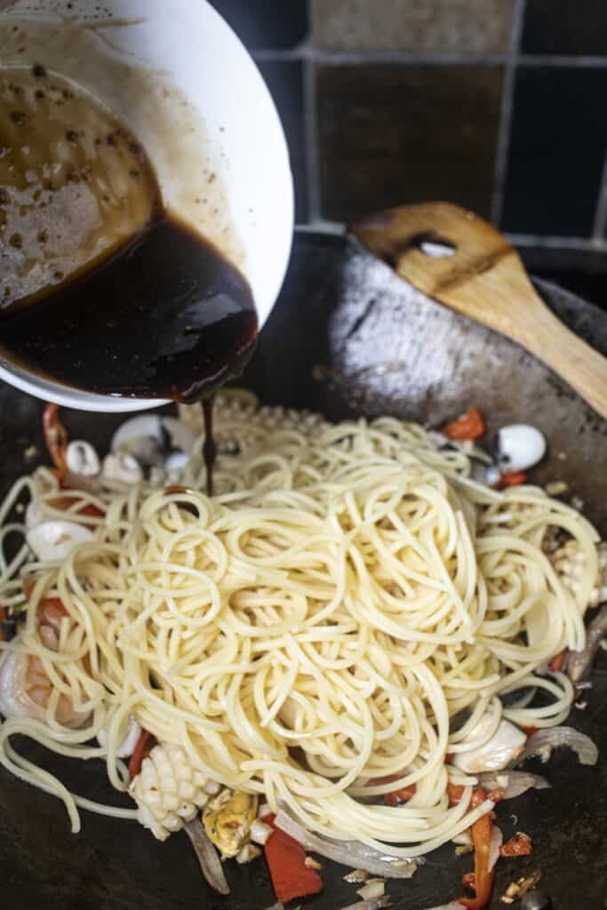 Sauce pouring into spaghetti noodles in a wok. 