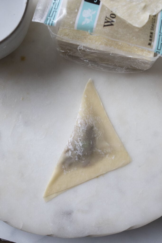 Triangular wrapped wonton on a cutting board. 