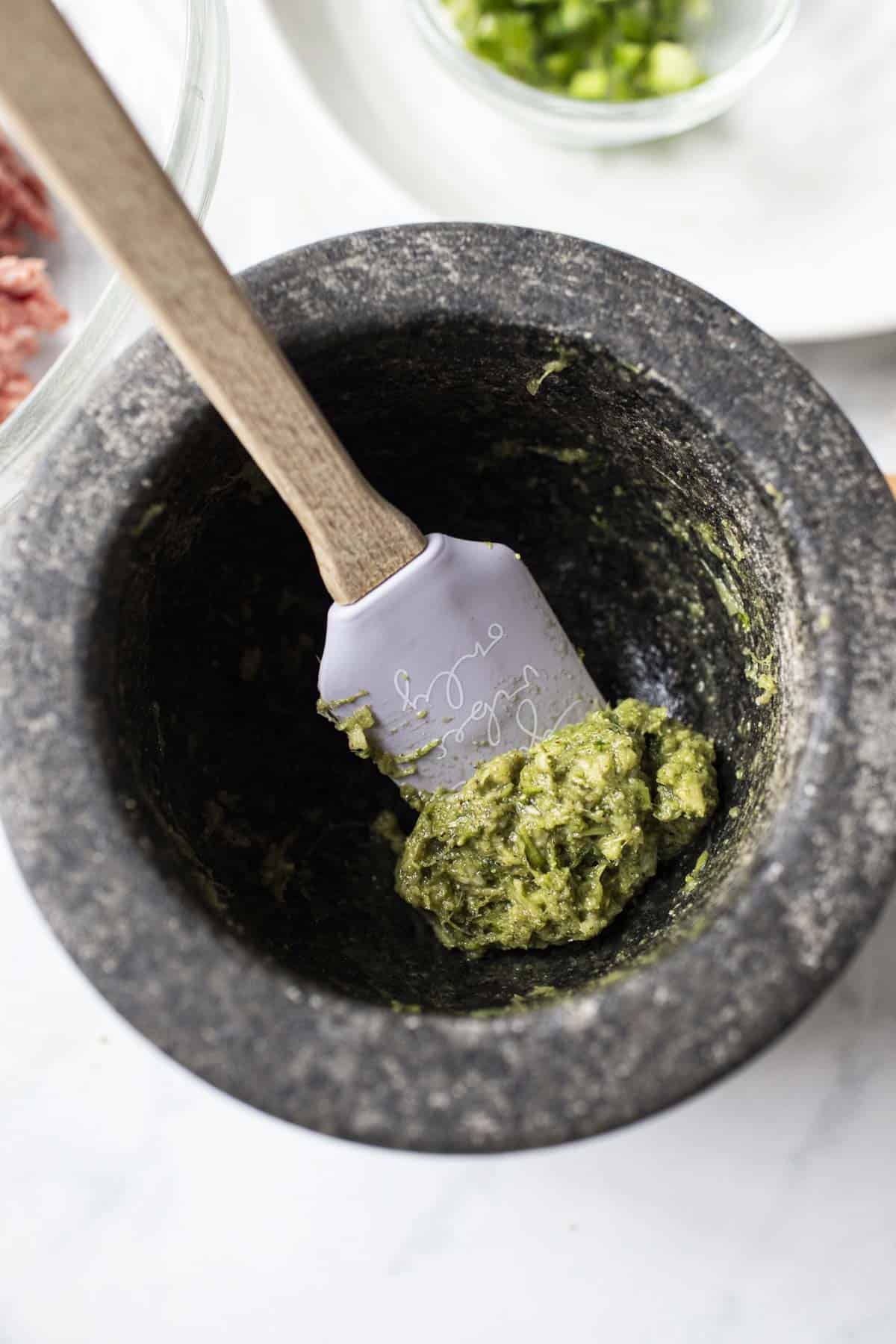 Spatula lifting green paste in a mortar.