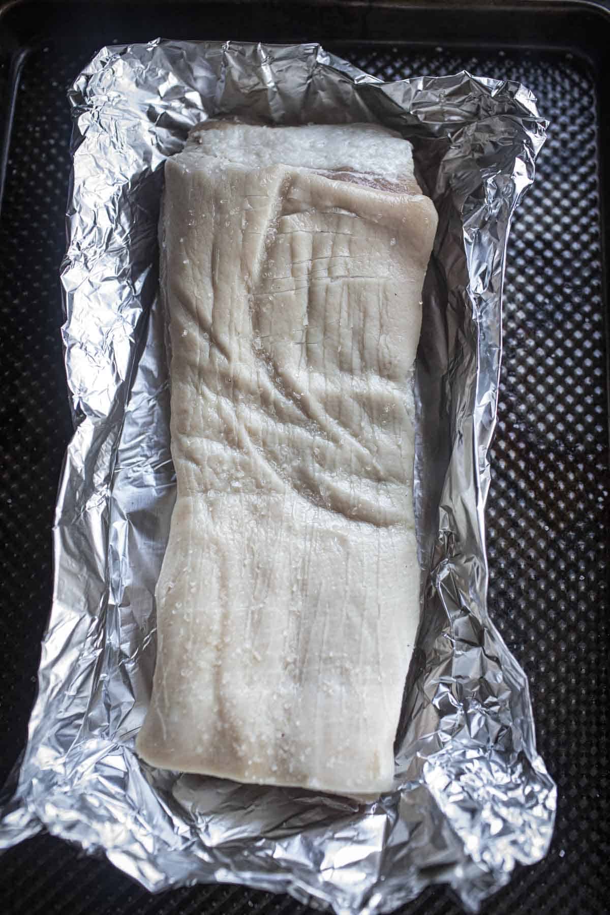 A piece of pork belly on foil on baking sheet. 