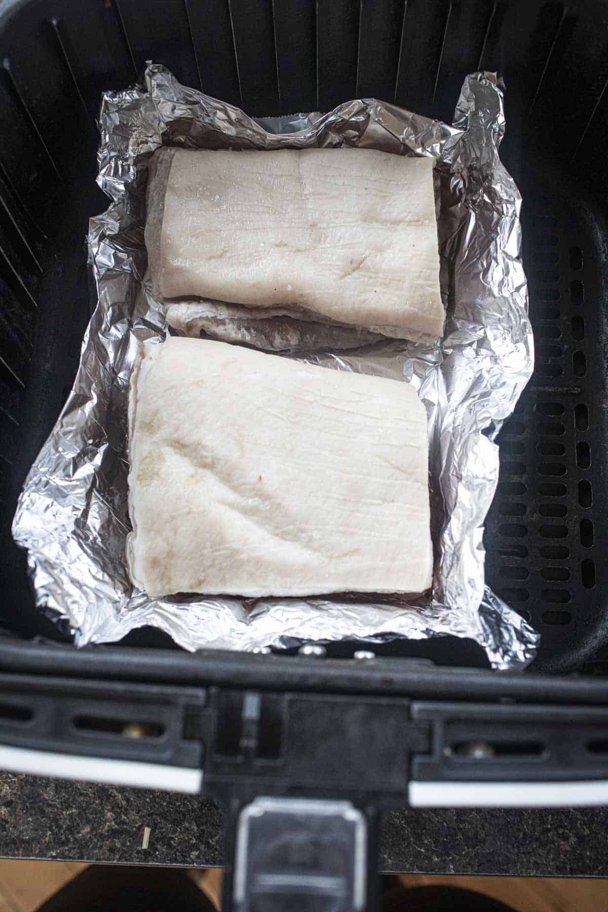 2 slices of raw pork belly over a foil in an air fryer.