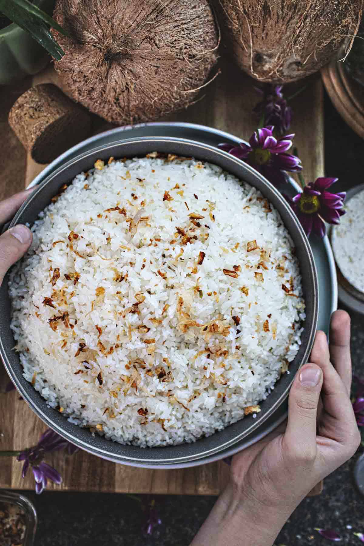 Hands holding coconut rice in a bowl.