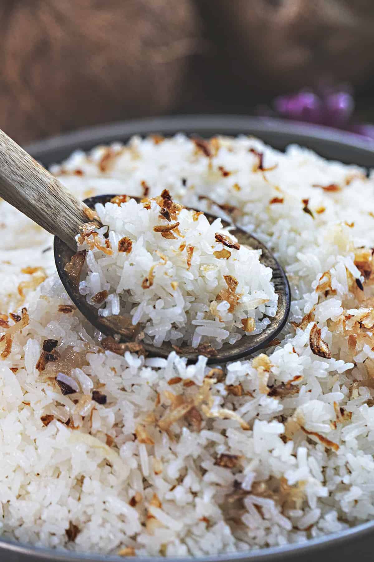 A wooden spoon lifting coconut rice from a bowl.