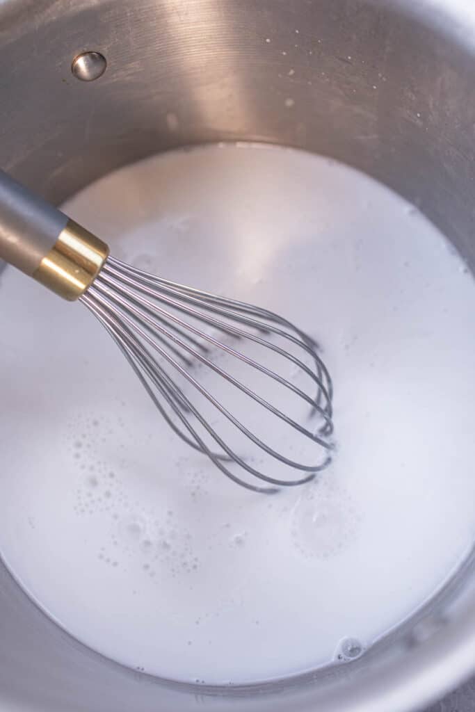 A whisk in a pot of coconut milk in a pot. 