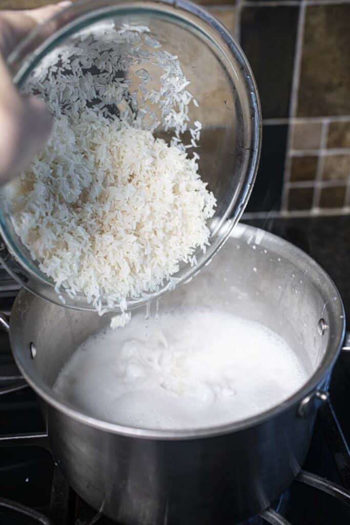 Rice pouring into a pot of coconut milk in a pot. 