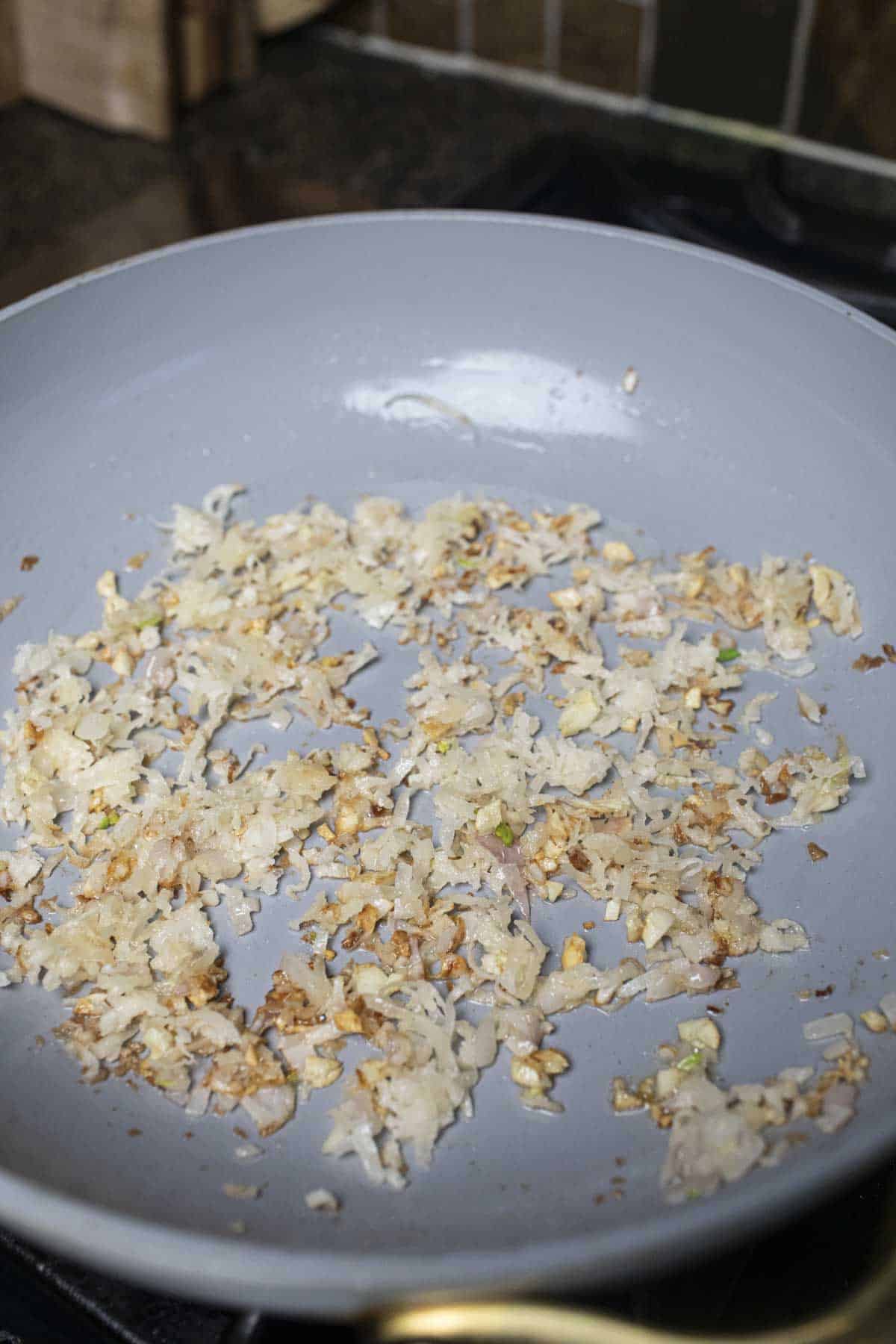 Sauteed onion, garlic, and shreded coconut in a pan.