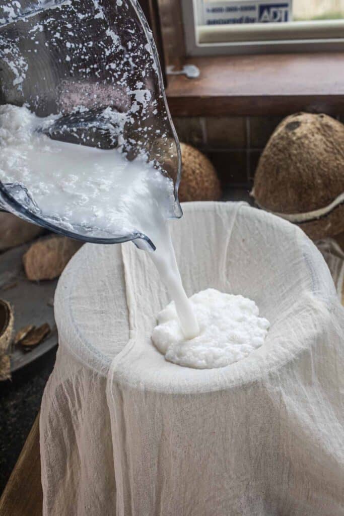 Coconut mixture pouring from food processor into cheesecloth. 