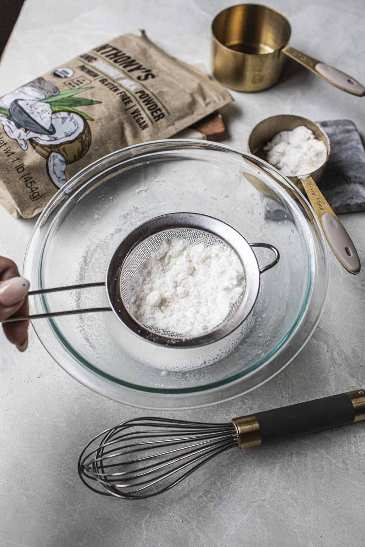 Wire mesh strainer straining  coconut powder over a bowl. 