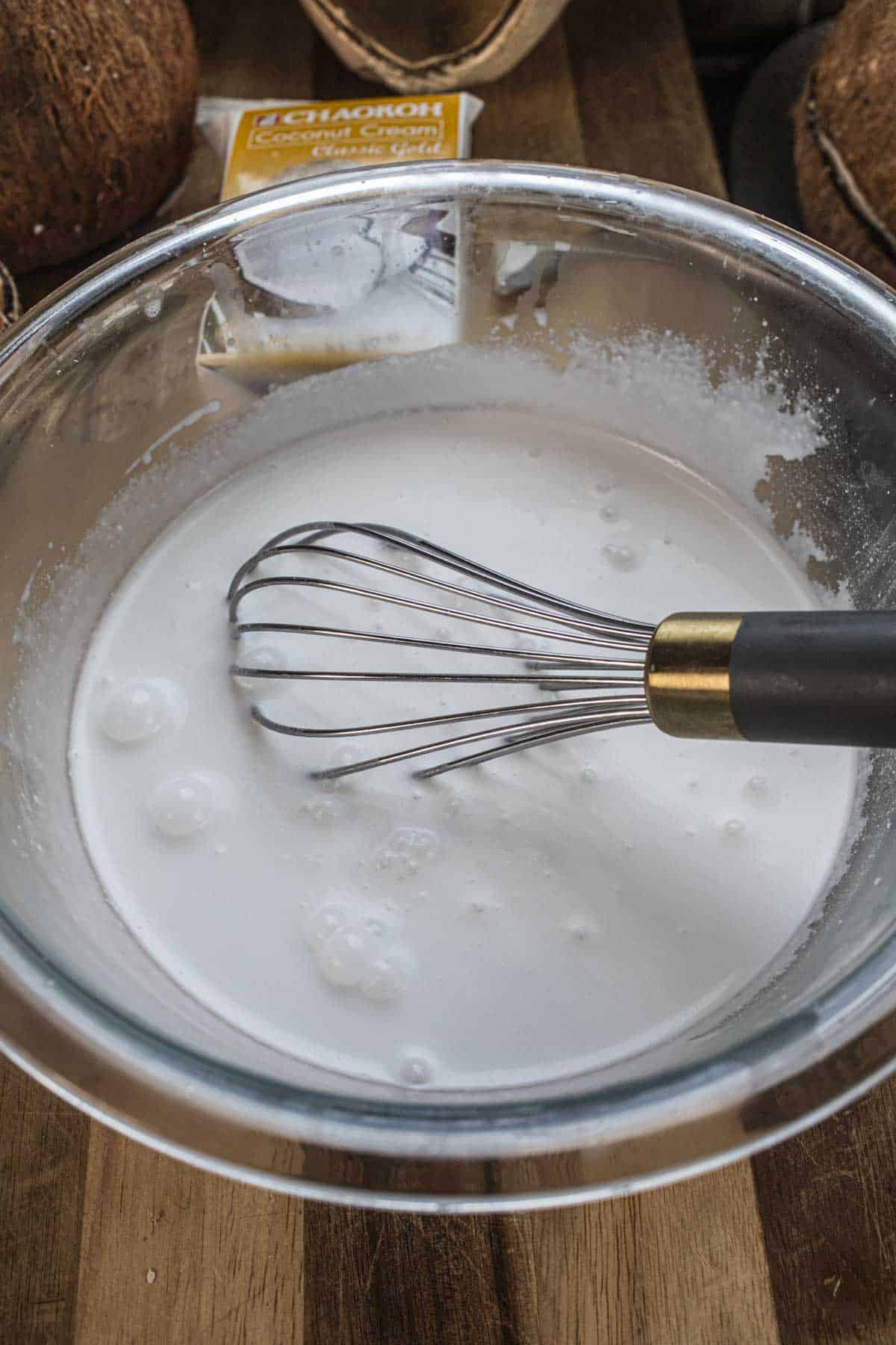 A whisk inside a bowl of coconut cream. 