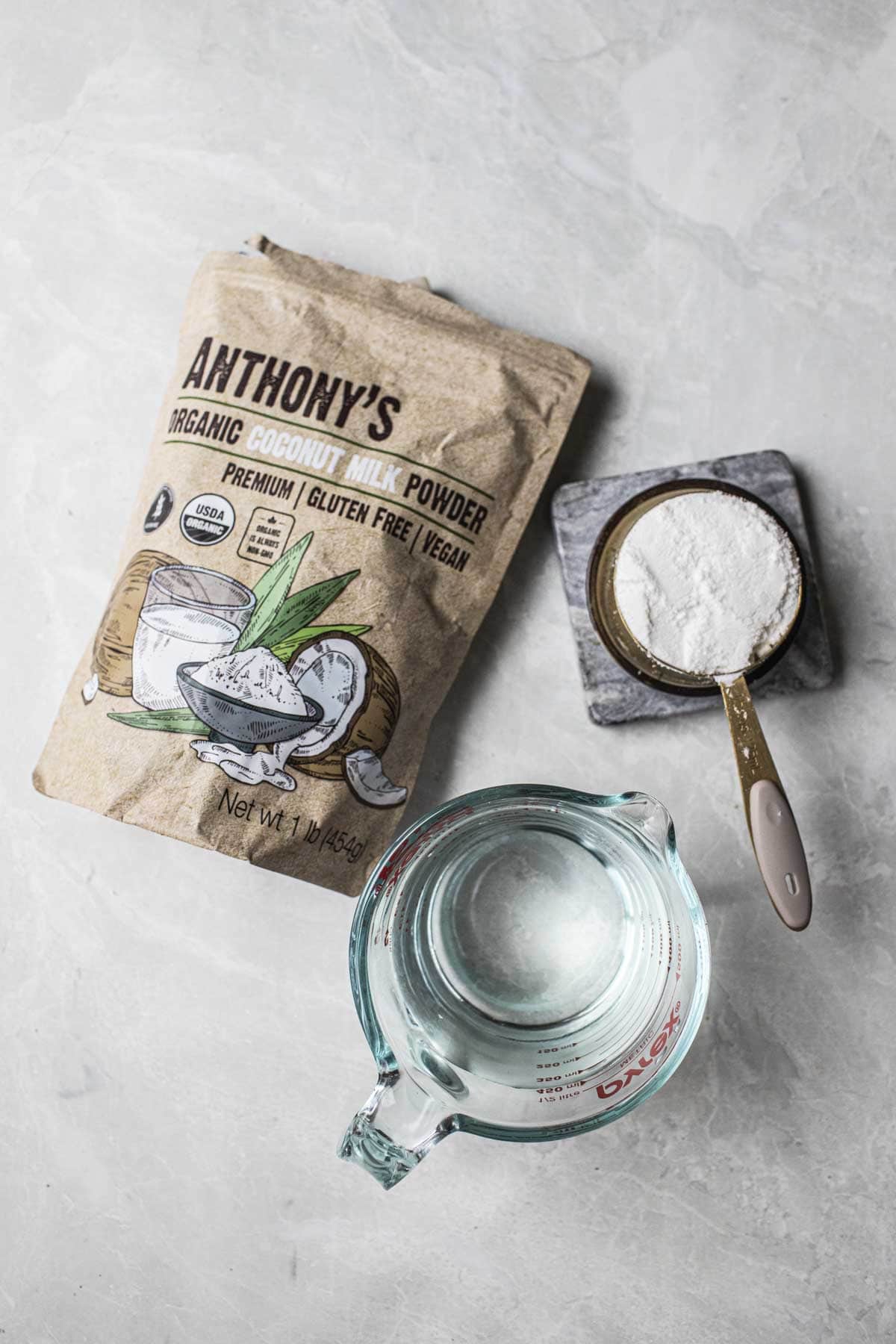 Coconut powder in a measuring cup and bag and water on the table.