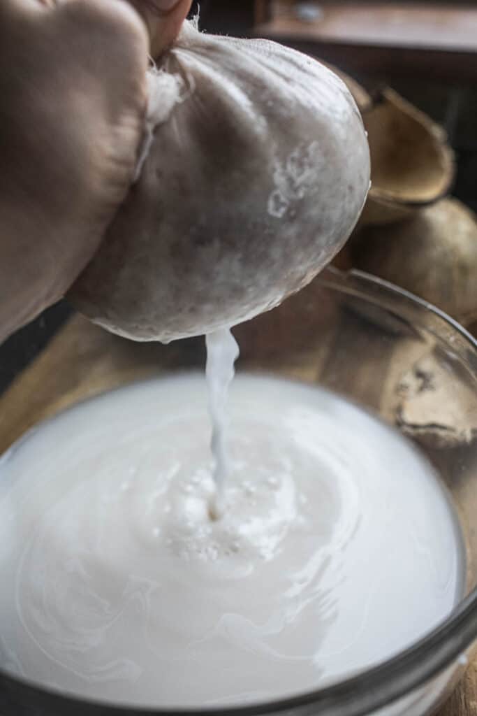 Coconut milk dripping from cheesecloth into a bowl. 