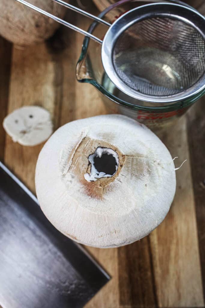 A hole on top of a young coconut on a cutting board.