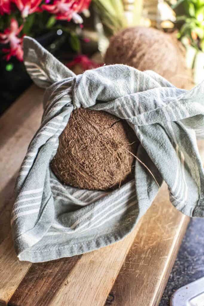 A towel wrapped around a coconut on a cutting board. 