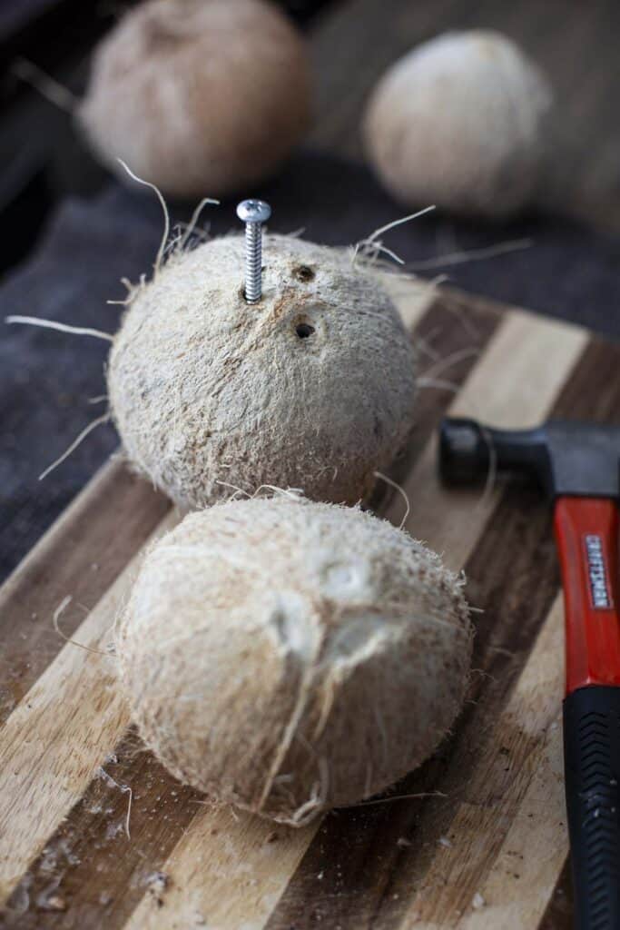 2 coconuts on a cutting board and one with screw on the eyelet.