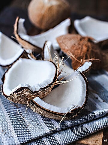 cracked coconuts on a cutting board next to knife.