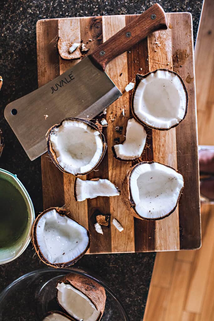 Cracked mature coconut on a cutting board with a cleaver.