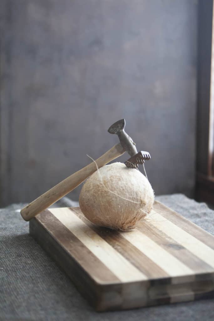 A vintage hammer on top of a coconut on a cutting board. 