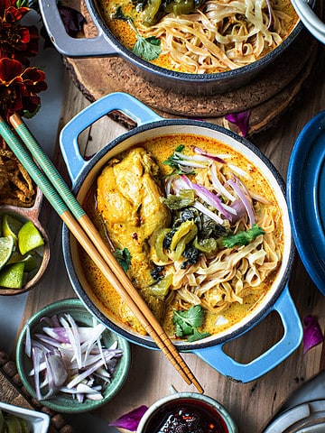 khao soi noodles in a blue bowl with chopsticks on top.