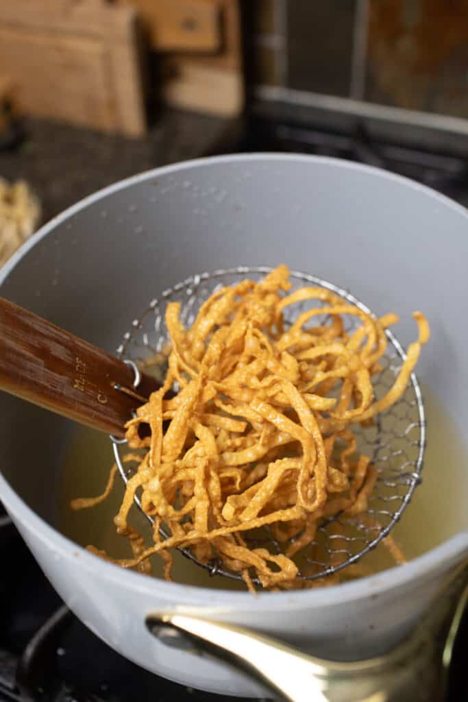 Wiremesh lifting crispy fried Chiang mai noodles from oil.