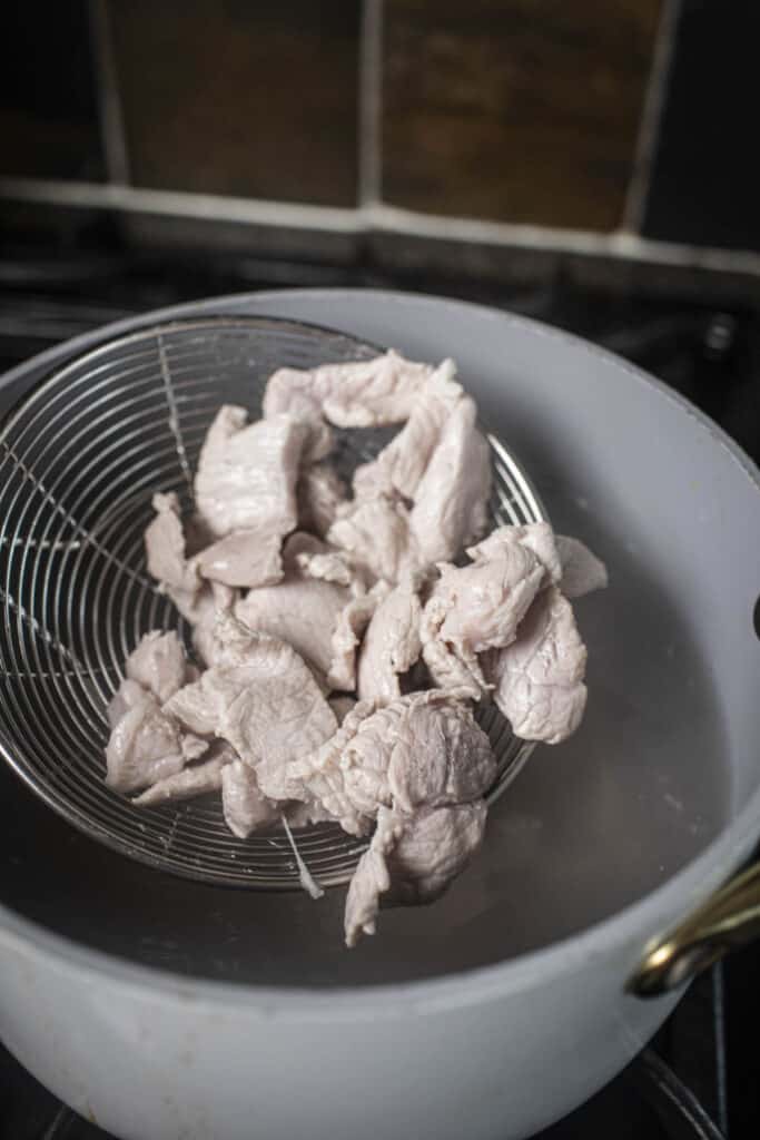 Wire mesh skimmer with cooked pork slices over a pot.