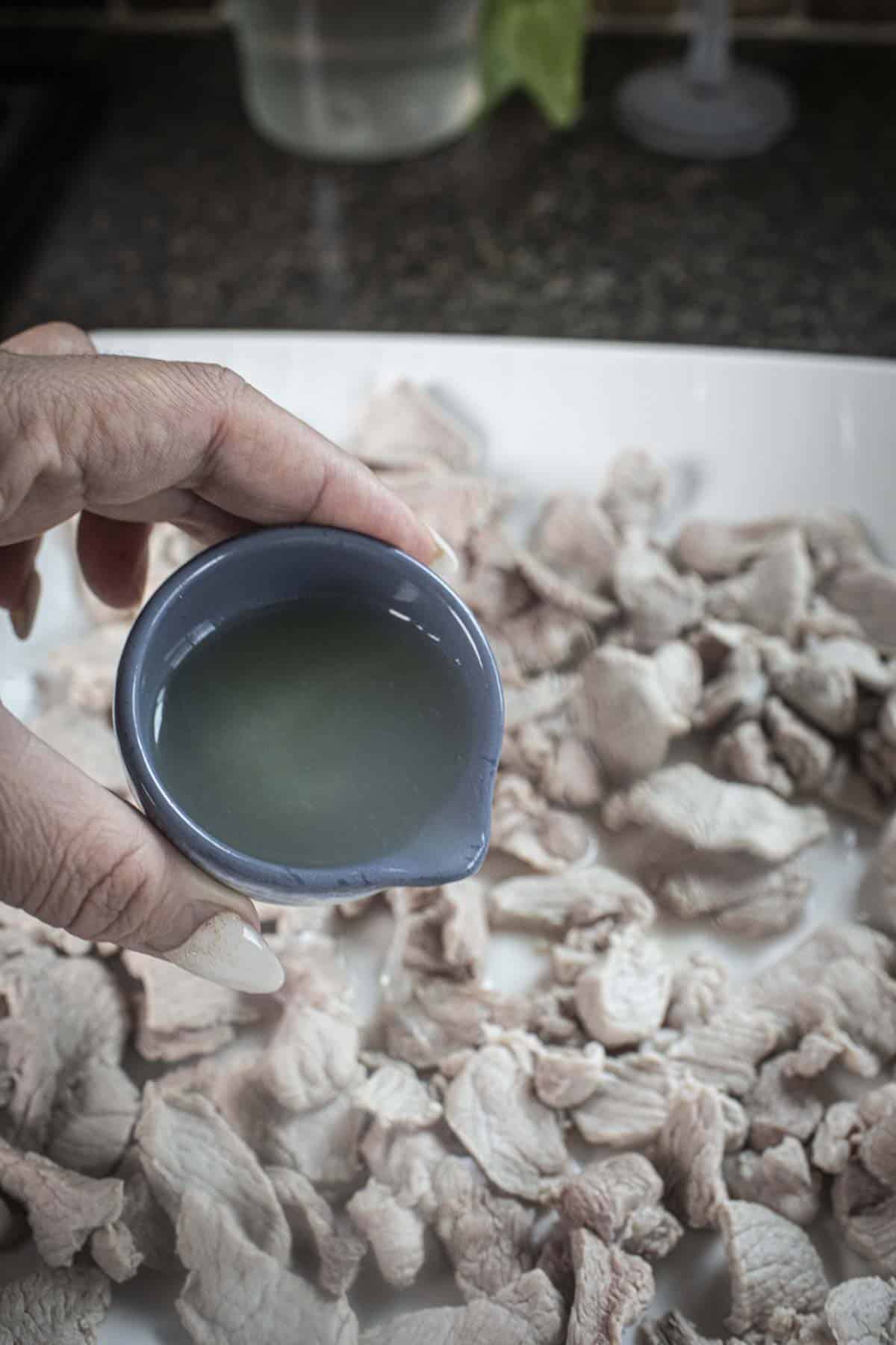 Lime juice pouring over pork slices on a white plate.