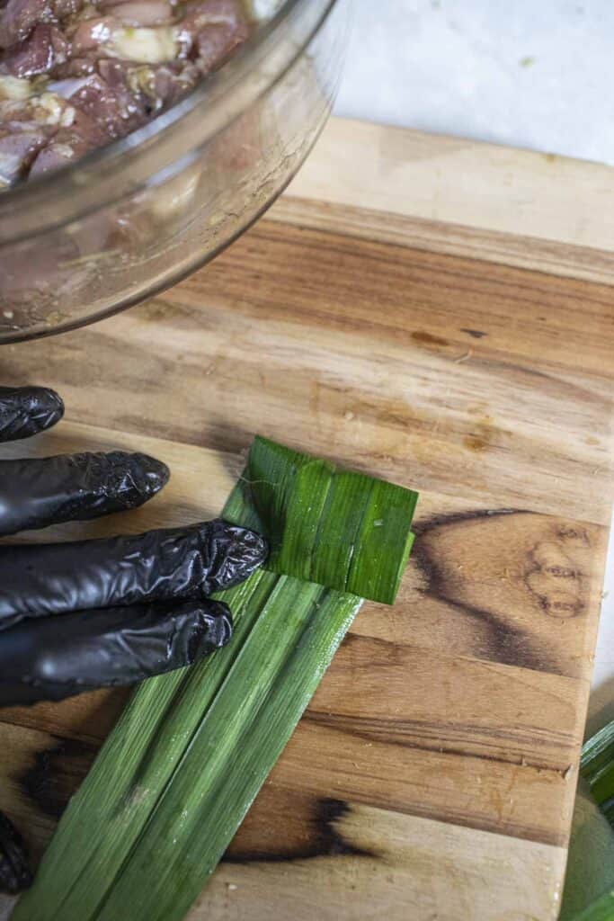 Hand rollin  pandan leave wrapped chicken on a cutting board. 