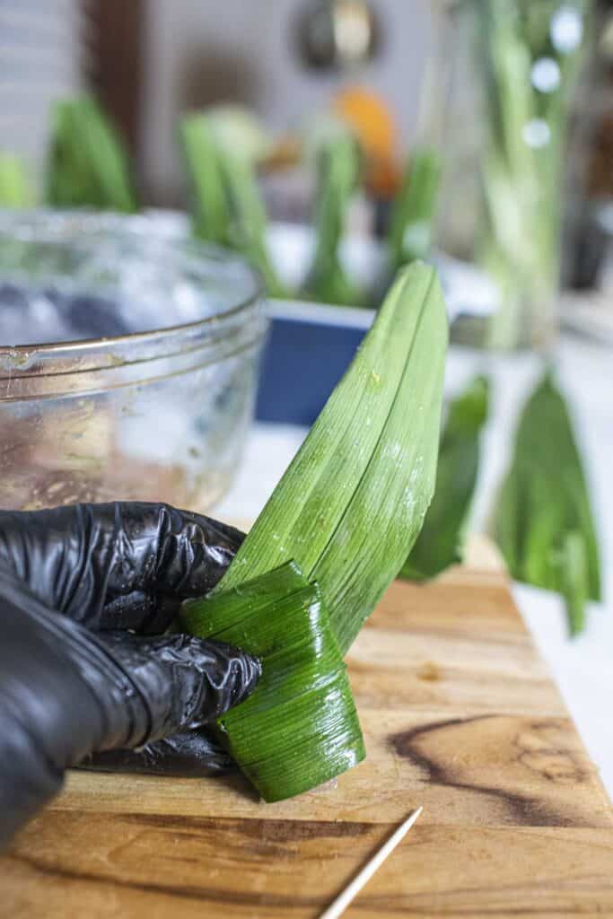 Hand holding  pandan leave wrapped chicken on a cutting board. 